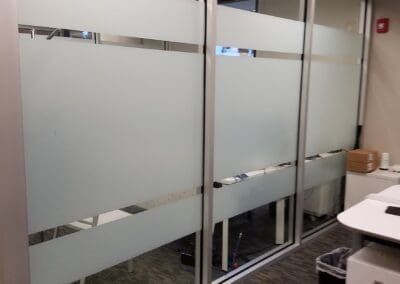 Office space with frosted glass partitions and a view of desks and a filing cabinet.