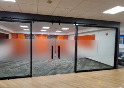 A modern office space featuring glass partition doors with frosted panels and orange accents.