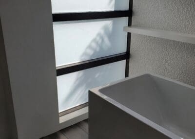 Modern bathroom corner with a white freestanding bathtub and window providing natural light.